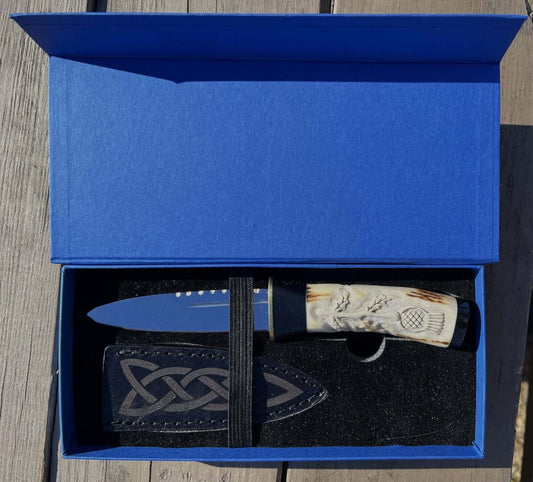 A hand forged Sgian Dubh with carbon steel blade with a hand-carved deer antler handle, presented in a blue display box with a cow leather sheath.