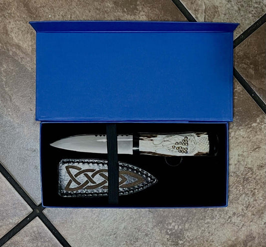 A hand-carved antler Sgian Dubh knife with a blade made of tempered carbon steel, displayed in a beautiful blue gift box with a cow leather sheath.