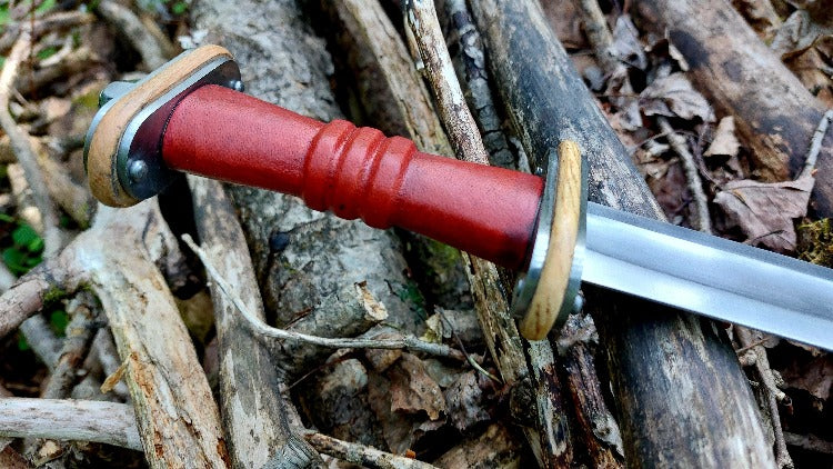 A Migration Era sword with a red grip and a carbon steel blade, featuring a decorative design on the handle.