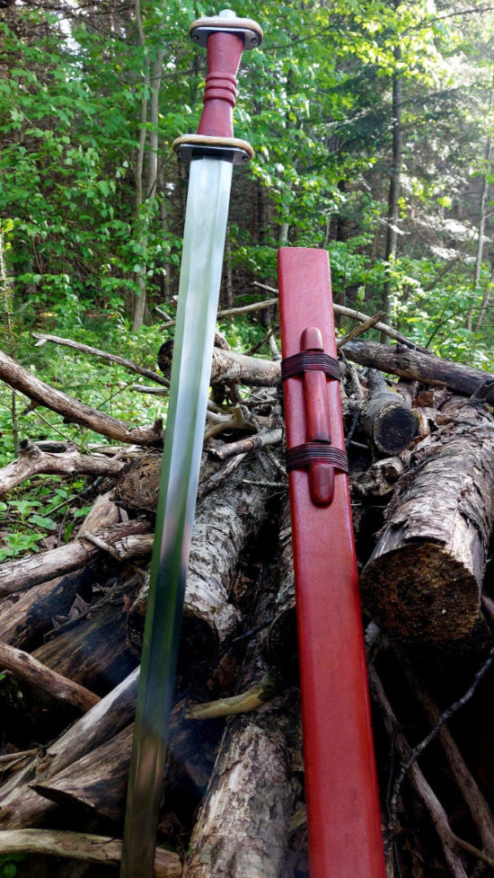 Sword with red sheath on a pile of logs in a forest setting