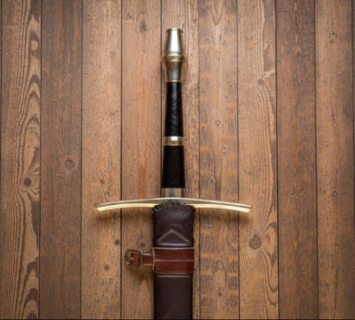 A hand forged steel sword with a green leather scabbard, laid on a green fabric surface.