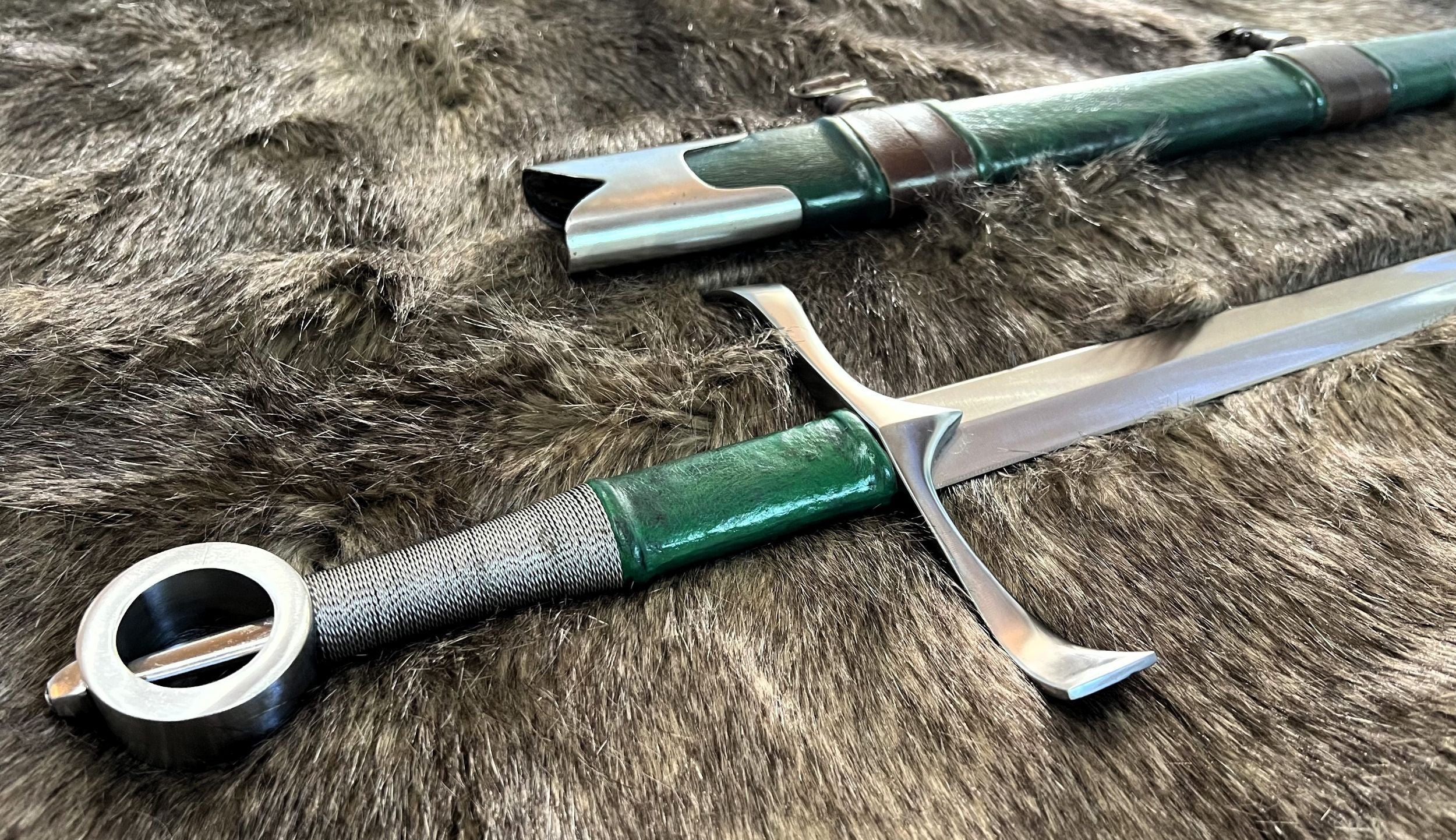 A hand and a half sword with a split grip of steel wire and green leather color scheme, featuring a wooden grip and a scabbard wrapped in green cowhide leather, placed on a furry surface.