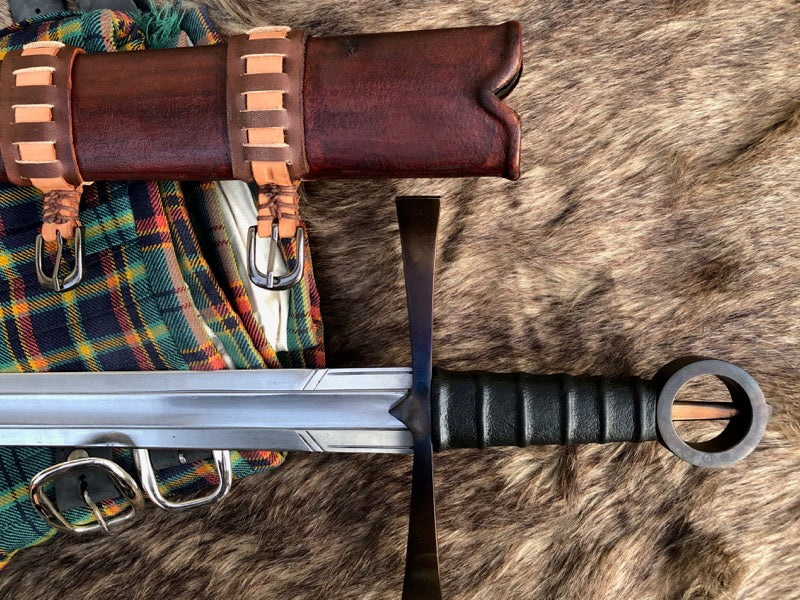 An Irish single hand ring hilt sword with a leather wrapped grip, displayed on a wooden scabbard with leather accents, lying on a fur surface.