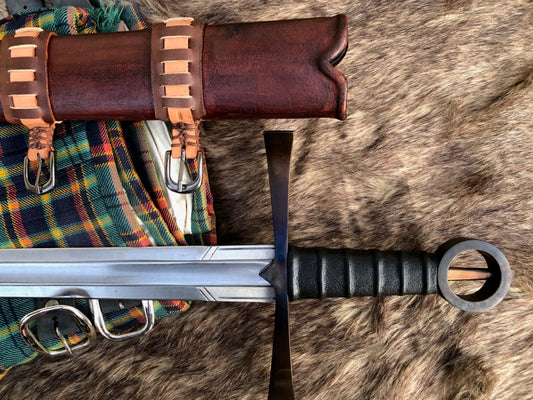 An Irish single hand ring hilt sword with a leather wrapped grip, displayed on a wooden scabbard with leather accents, lying on a fur surface.