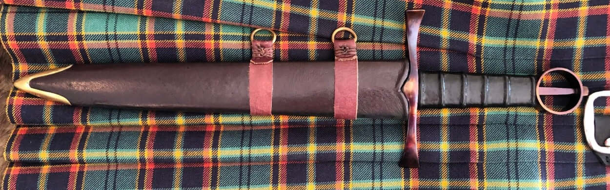 Irish Kern companion dagger displayed on traditional tartan fabric, featuring a detailed scabbard and handle.