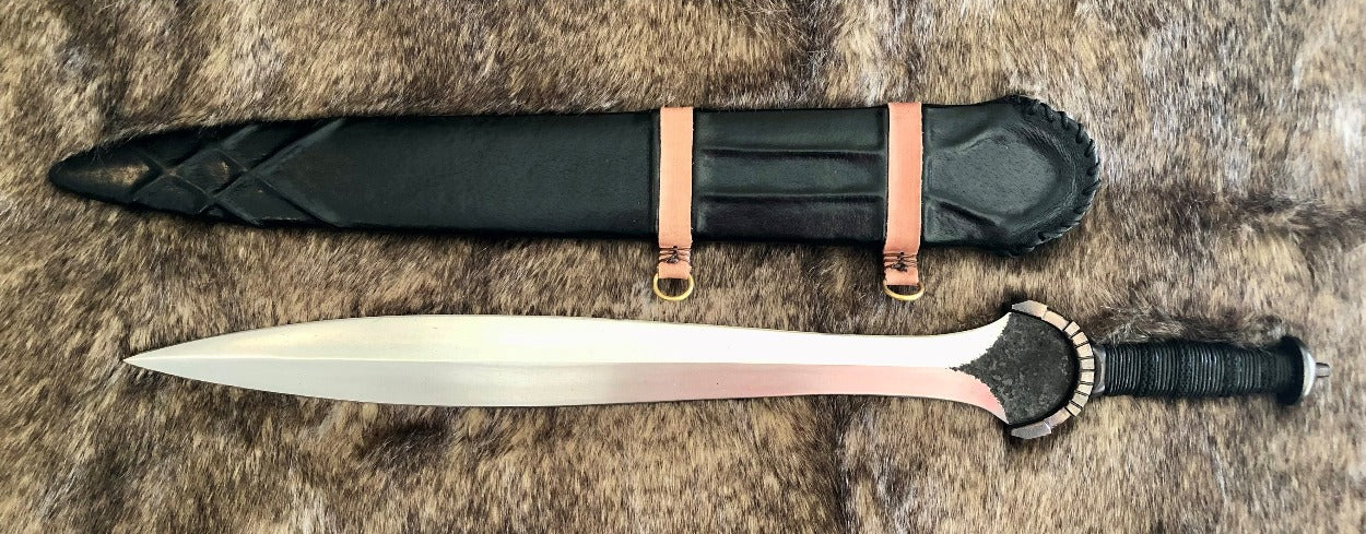 A hand forged carbon steel blade with a leaf design, featuring a full tang construction. The blade is accompanied by a wooden scabbard wrapped in leather, with leather accents on the handle.