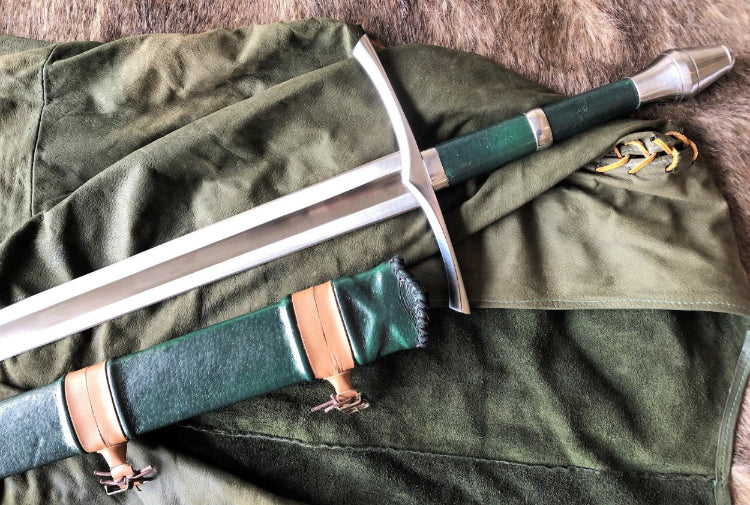 A hand forged steel sword with a green leather scabbard, laid on a green fabric surface.