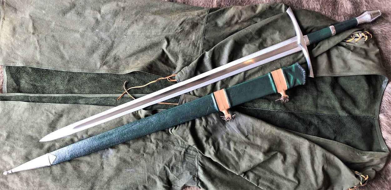 A hand forged steel sword with a green leather scabbard, laid on a green fabric surface.