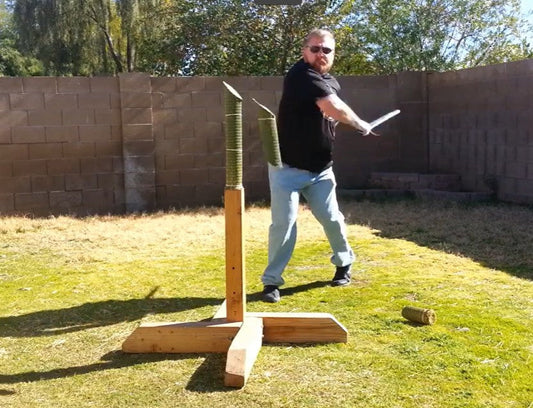 A practitioner demonstrating cutting techniques with hand forged medieval swords for HEMA on a cutting stand outdoors.