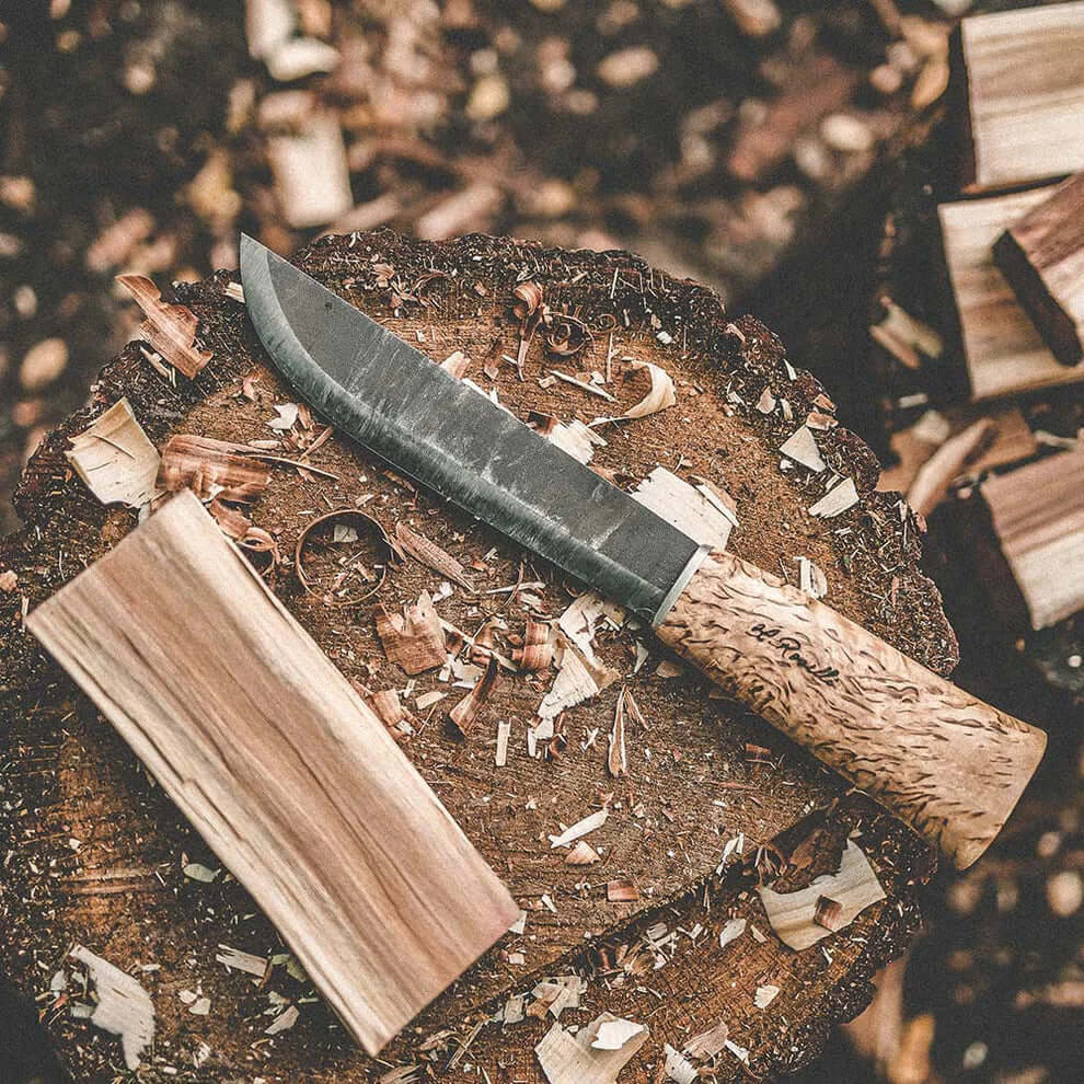 Roselli R150 The Big Leuku Knife - Sami Camp Knife placed on a wooden log with shavings around it.