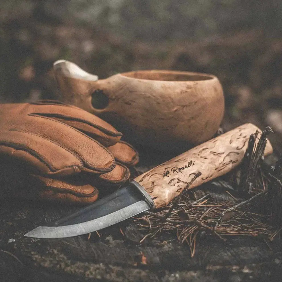 Roselli Hunter R100 knife with a curly birch handle and a handmade leather sheath alongside gloves and a wooden bowl.
