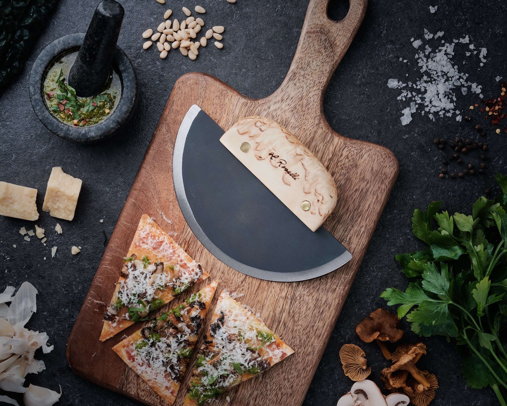 Roselli R740 The Ulu Knife on a wooden cutting board with pizza slices and ingredients around it.