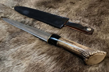 Crown stag Scottish dirk with Damascus blade, on a fur surface.
