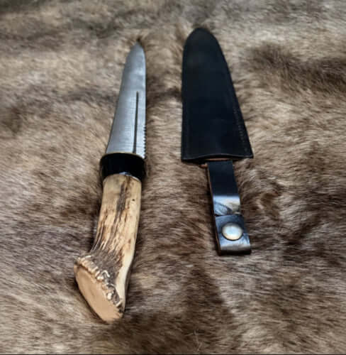 Scottish dirk with crown stag handle resting beside its leather sheath on fur