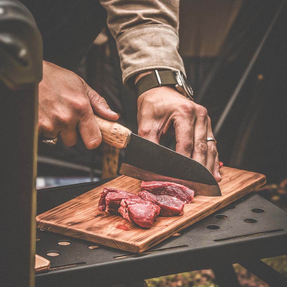 Person using Roselli R700 The Small Chef Knife to slice raw meat on a wooden cutting board