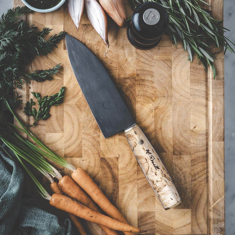 Roselli R760 The Santoku Knife on a wooden cutting board with fresh vegetables and herbs.