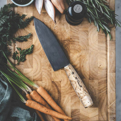 Roselli R760 The Santoku Knife on a wooden cutting board with fresh vegetables and herbs.