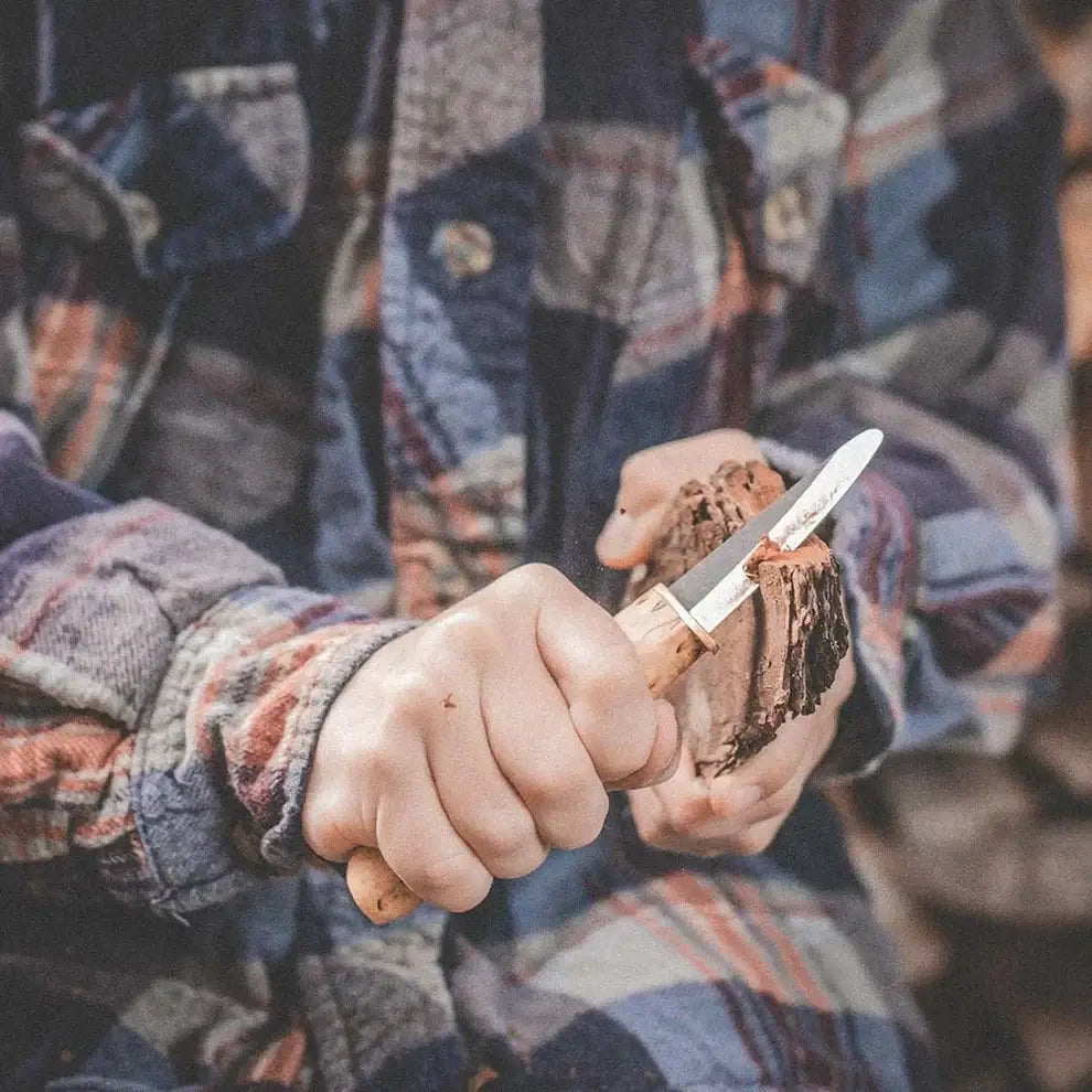 Child using the Roselli R140 The Little Carpenter knife to carve wood outdoors.